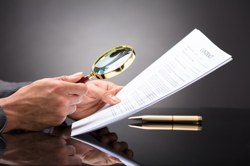 Person examining a contract with a magnifying glass.