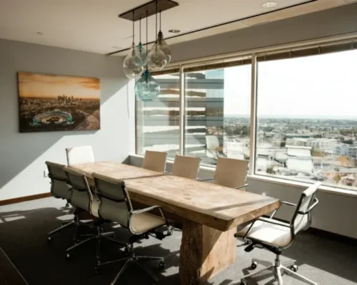 Sunlit conference room with a long wooden table and windows overlooking the city.