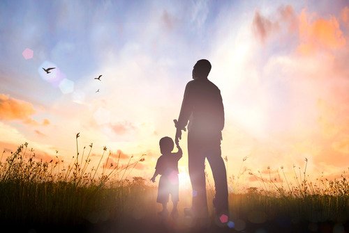 Adult and child holding hands at sunset.